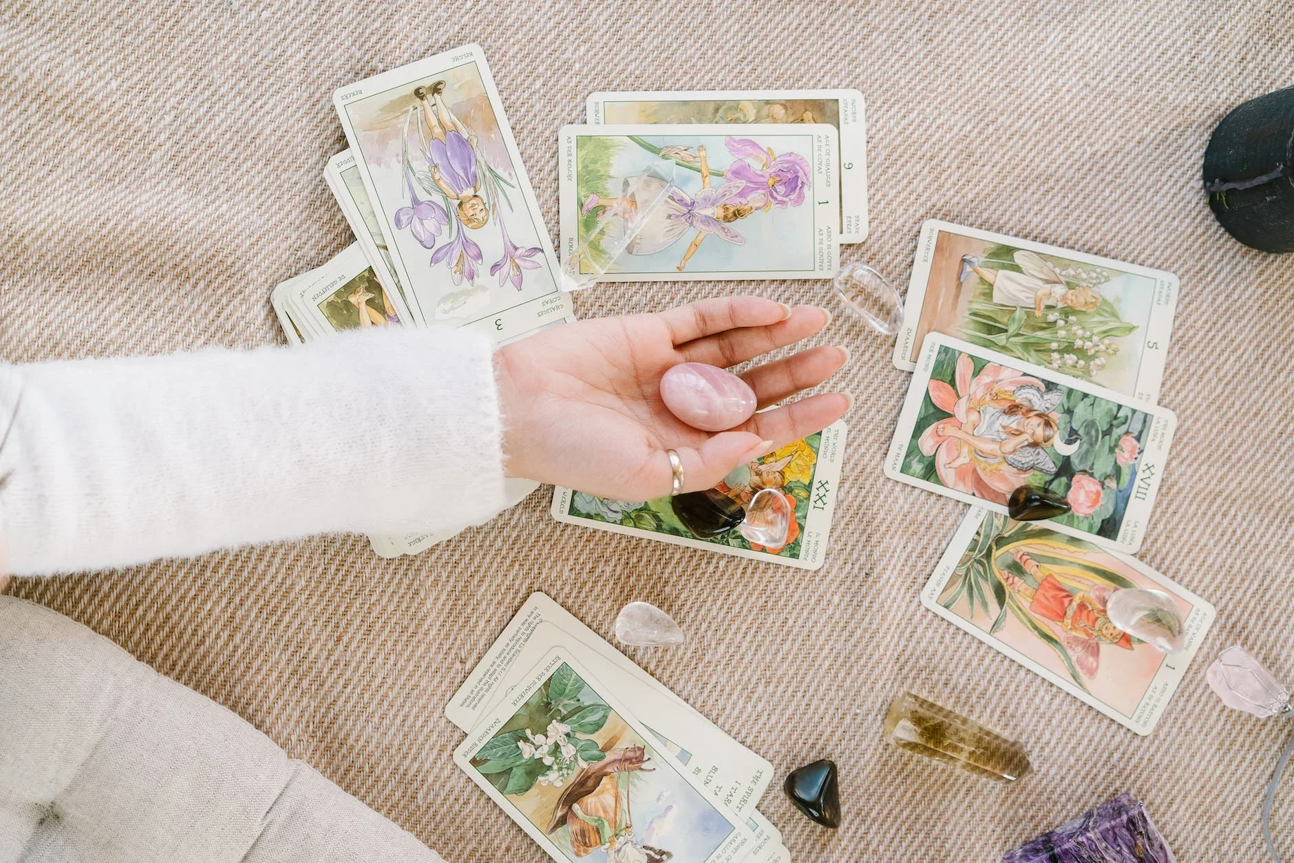 A person holds a crystal in their hand above a reading of tarot cards.