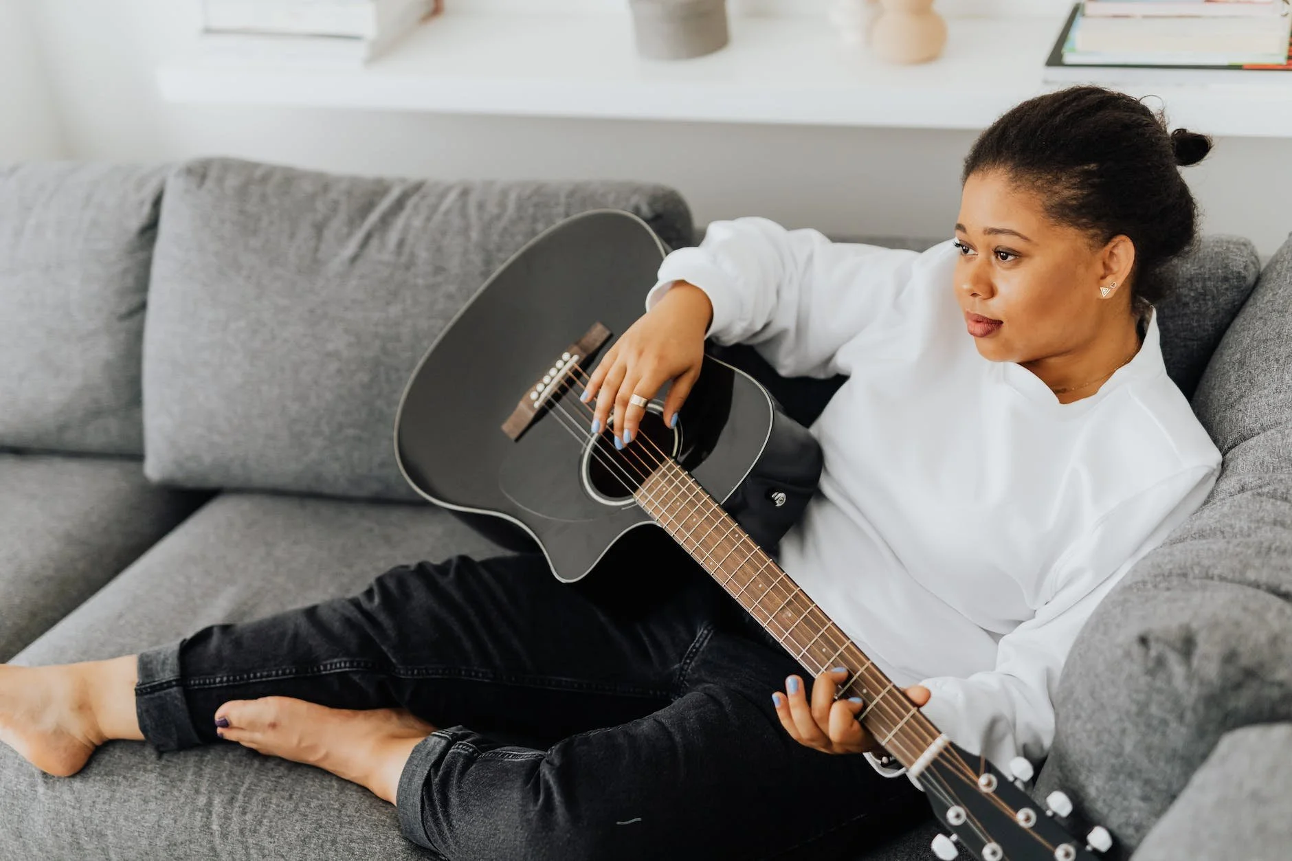 Person sits on the couch strumming an acoustic guitar