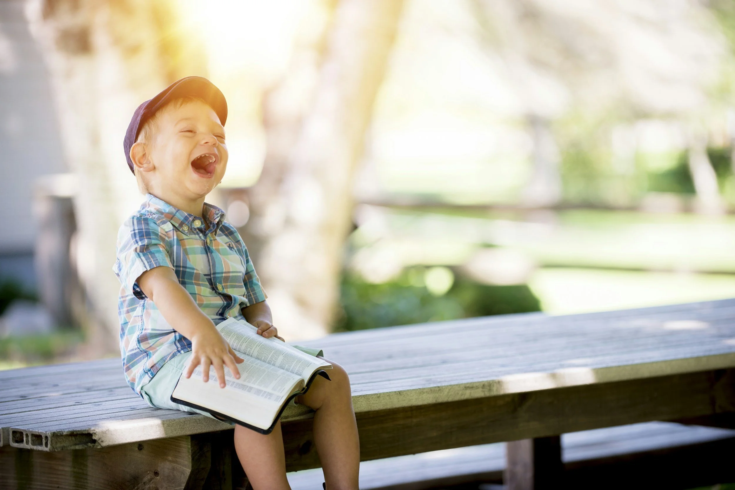 Happy child smiling and laughing, holding a Bible as he sits at the table.