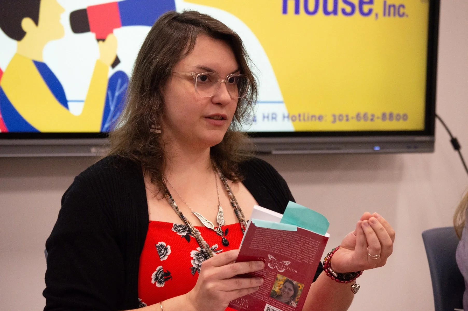 Safrianna holding a book and speaking to a crowd.